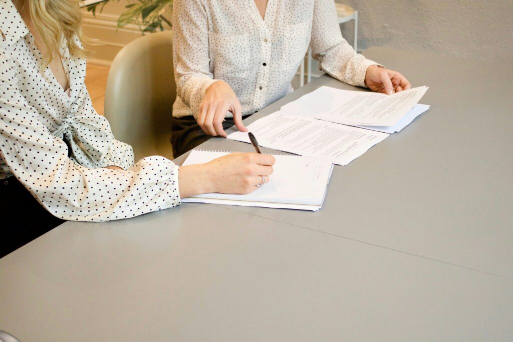 Two women sit at a table with paperwork in front of them